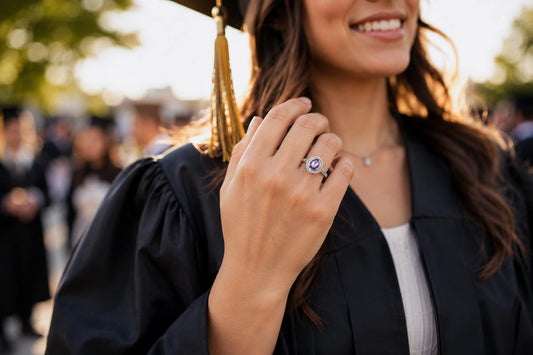 Smiling graduate wearing a personalized birthstone class ring during graduation ceremony, celebrating a major academic achievement.