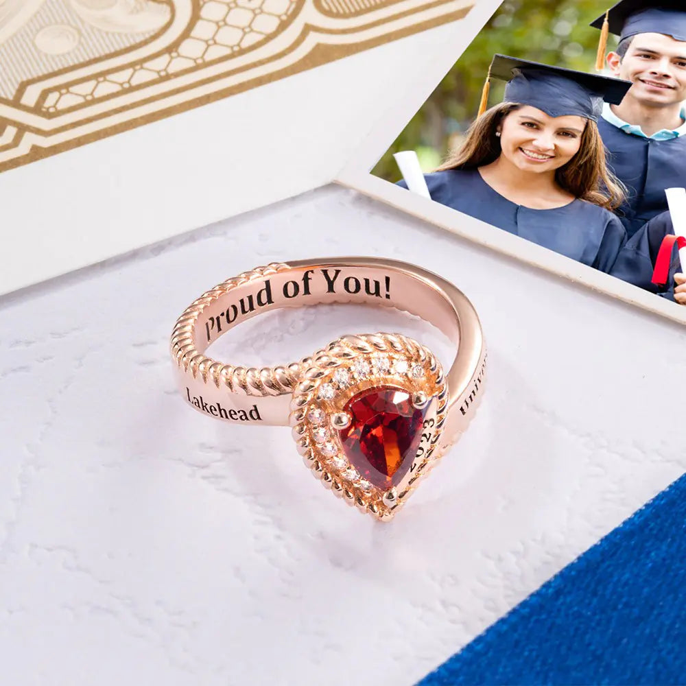 Rose gold personalized graduation ring with red heart birthstone and engraved message “Proud of You”