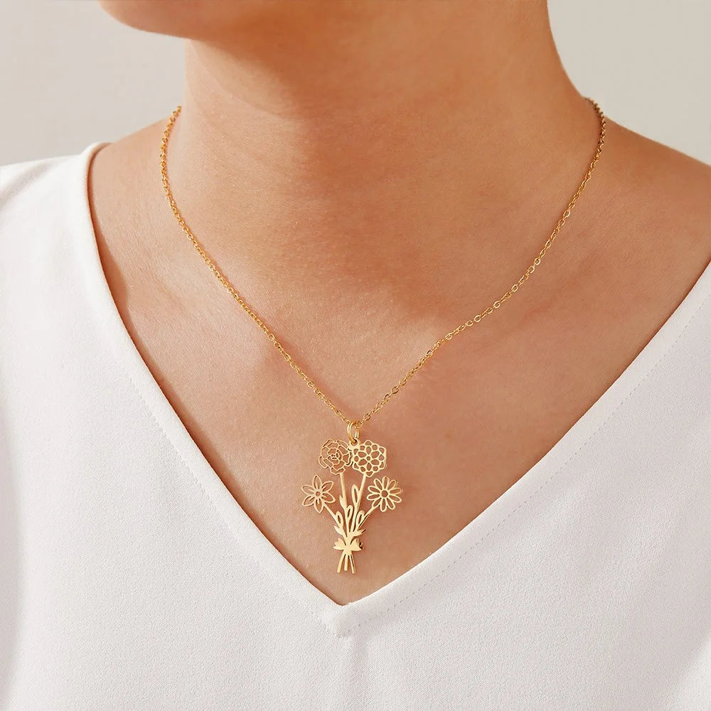 Gold necklace with a floral pendant worn by a person in a white top on a neutral background