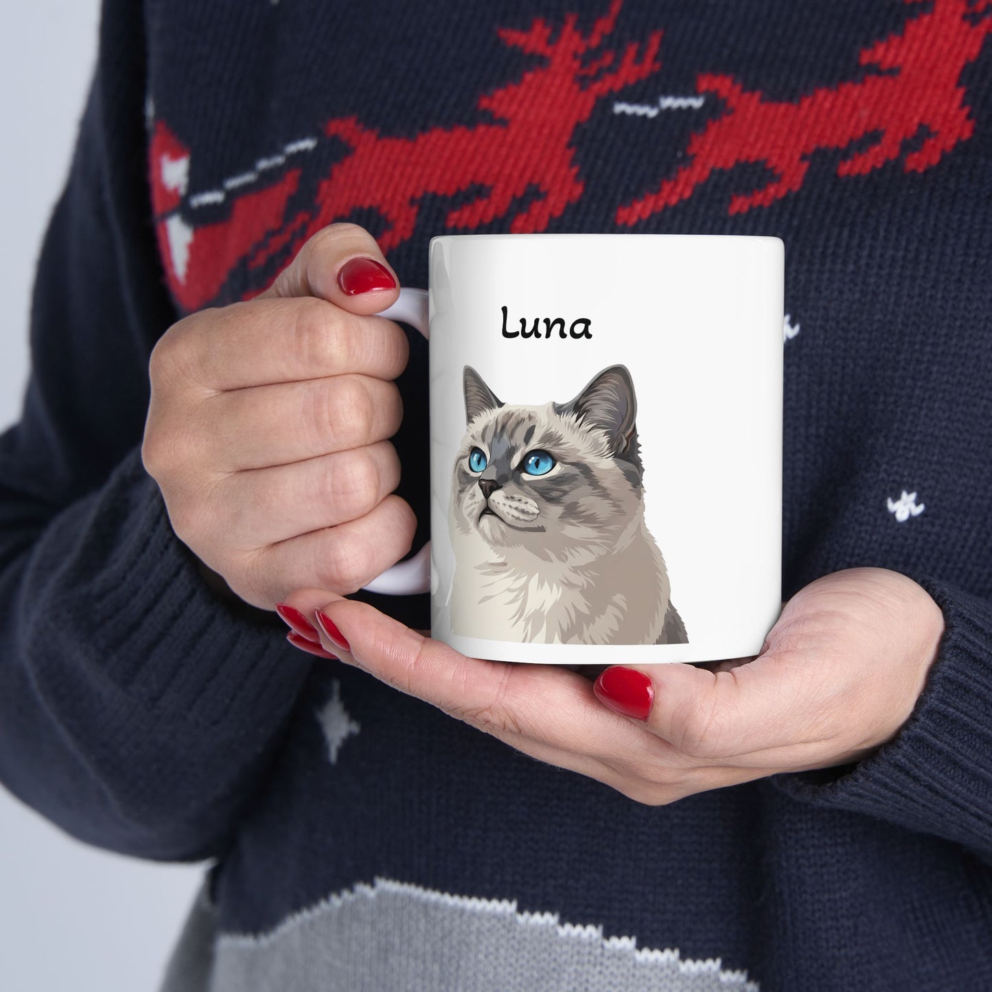 Person holding a mug with a cat illustration and 'Luna' text, wearing a sweater with reindeer design.