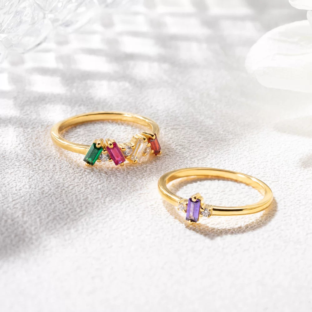 Two custom baguette birthstone rings in gold, showing different personalized stone combinations