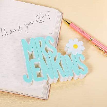 Light blue personalized 3D teacher name sign with a flower icon displayed on an open notebook