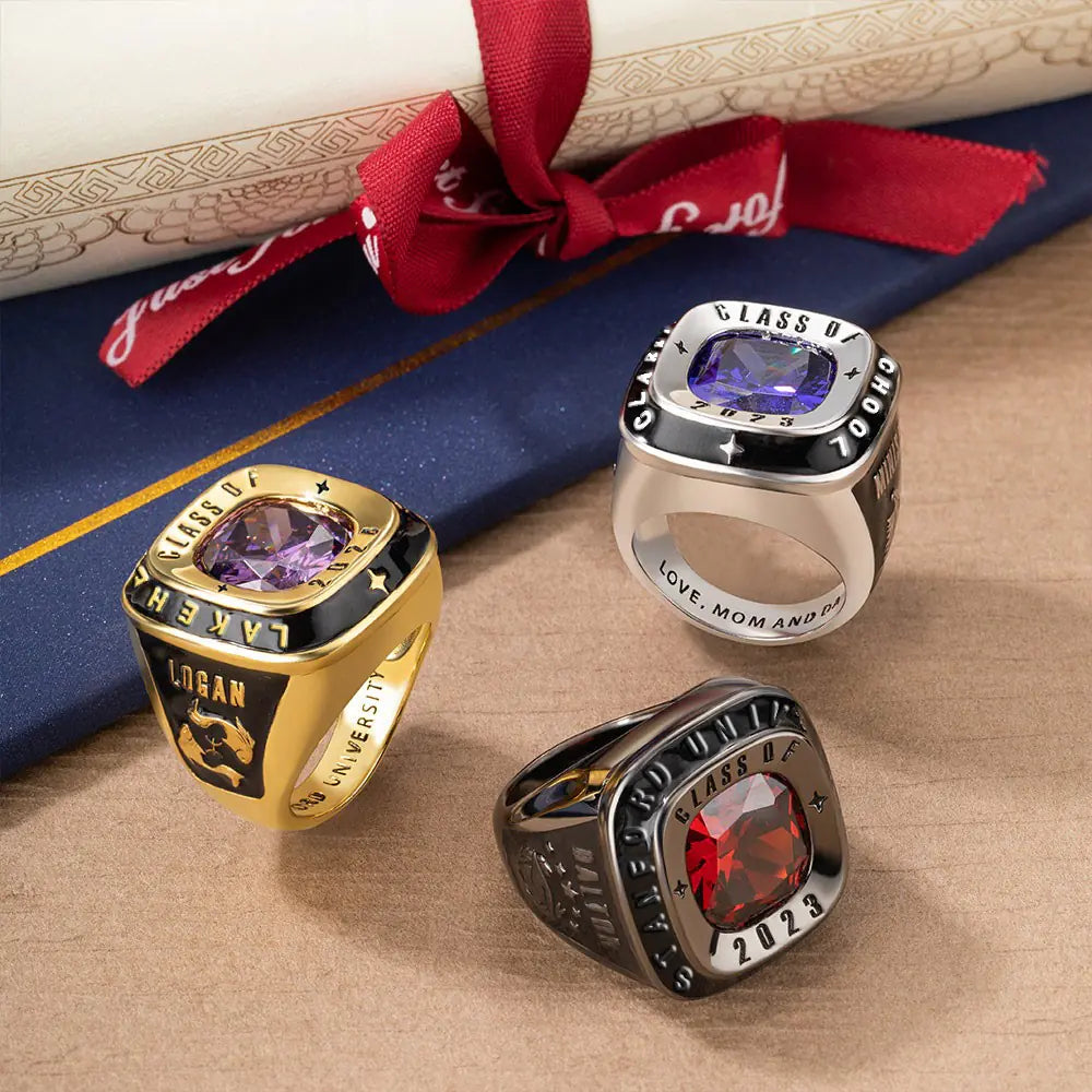 Three custom class rings for men displayed on a graduation backdrop, featuring personalized engravings and precious stones.