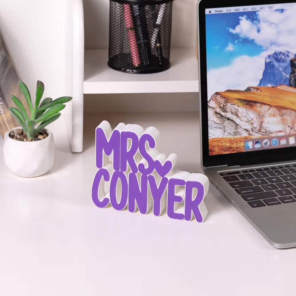 A custom purple and white 3D lettered sign spelling 'MRS. CONYER' sits on a white desk next to a laptop and a small potted succulent.